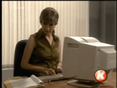 A Woman Sits At A Desk Typing On A Keyboard In Front Of A Computer With A Red K On The Bottom Right GIF