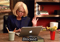 A Woman Sits At A Desk With An Apple Laptop And The Word Blocked On The Table GIF