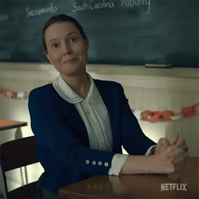 A Woman Sits At A Desk With Her Hands Folded In Front Of A Blackboard That Says South Carolina On It GIF