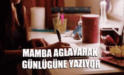 A Woman Sits At A Desk Writing In A Notebook And The Words Mamba Aglayarak Gunlugune Yaziyor Are Above Her GIF