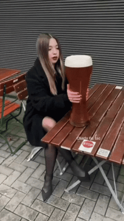 A Woman Sits At A Table Holding A Giant Beer Glass GIF