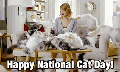A Woman Sits At A Table Surrounded By Cats With The Caption " Happy National Cat Day " GIF