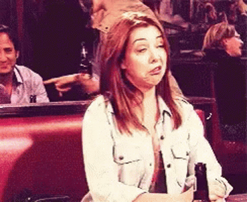 A Woman Sits At A Table With A Bottle Of Beer In Her Hand GIF