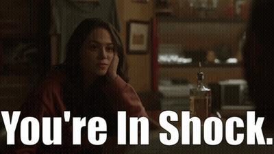 A Woman Sits At A Table With A Bottle Of Whiskey And The Words " You 'Re In Shock " Above Her GIF