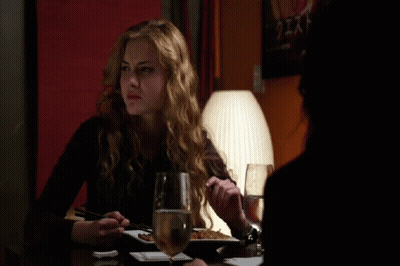 A Woman Sits At A Table With A Glass Of Wine And A Plate Of Food GIF