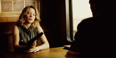 A Woman Sits At A Table With A Gun In Her Hand GIF