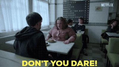 A Woman Sits At A Table With A Plate Of Food Next To A Sign That Says " Don 'T You Dare " GIF
