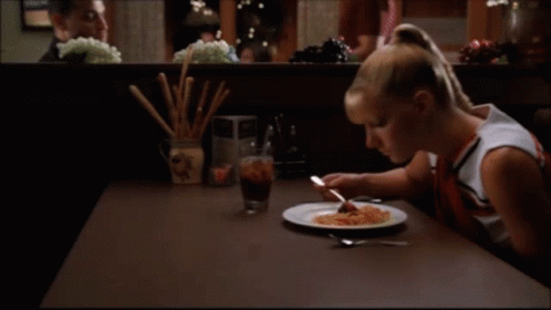 A Woman Sits At A Table With A Plate Of Food On It GIF