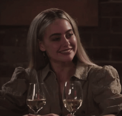 A Woman Sits At A Table With Two Glasses Of Wine In Front Of Her GIF