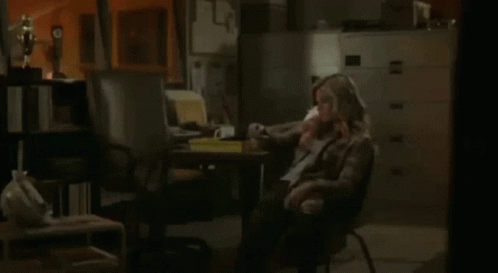 A Woman Sits In A Chair Talking On A Phone GIF