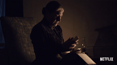 A Woman Sits In A Dark Room Reading A Book With A Netflix Logo On The Bottom GIF