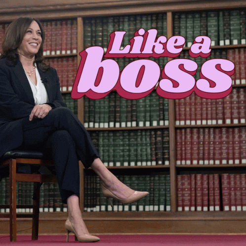 A Woman Sits In Front Of A Bookshelf With The Words Like A Boss Behind Her GIF