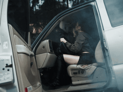 A Woman Sits In The Driver 'S Seat Of A Car With The Door Open GIF