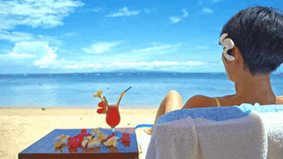 A Woman Sits On A Beach With A Drink On The Table GIF