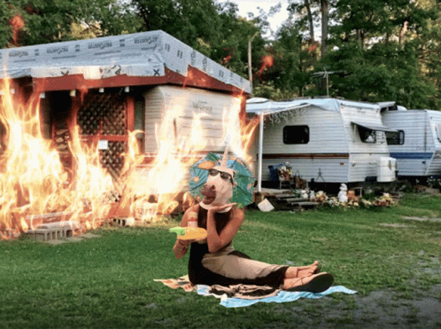 A Woman Sits On A Blanket In Front Of A Rv That Is On Fire GIF