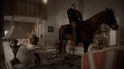 A Woman Sits On A Couch In A Living Room With Two Lamps GIF