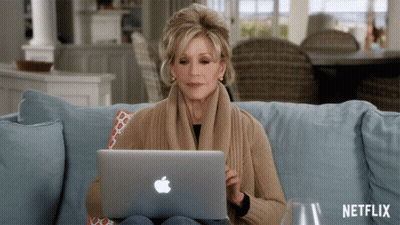 A Woman Sits On A Couch Using An Apple Laptop With Netflix Written On The Bottom GIF