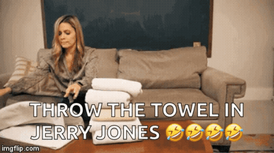 A Woman Sits On A Couch With A Stack Of Towels And The Words Throw The Towel In Jerry Jones Below Her GIF