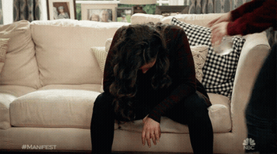 A Woman Sits On A Couch With Her Head On Her Knees And A Nbc Logo On The Bottom Right GIF