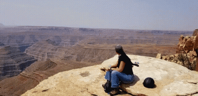 A Woman Sits On A Rock Overlooking A Desert Landscape GIF