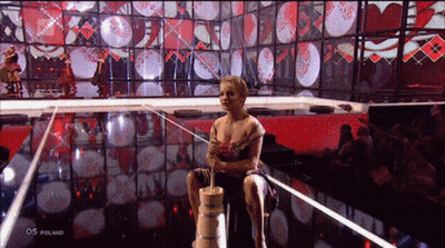 A Woman Sits On A Wooden Barrel In Front Of A Screen That Says 05 Poland On It GIF