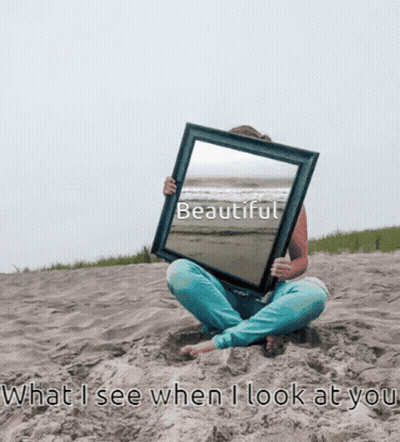 A Woman Sits On The Beach Holding A Picture Frame With The Word Beautiful On It GIF