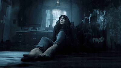 A Woman Sits On The Floor In A Dark Room Looking Up GIF