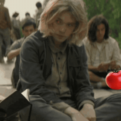 A Woman Sits On The Ground With A Red Tomato In The Foreground GIF