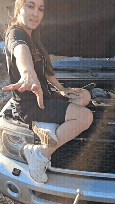 A Woman Sits On The Hood Of A Car With The Hood Open GIF
