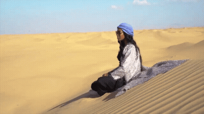 A Woman Sits On Top Of A Sand Dune GIF