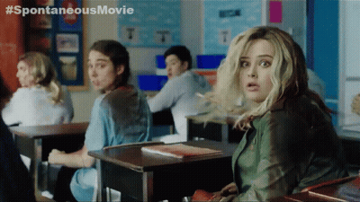 A Woman Sitting At A Desk In A Classroom With A # Spontaneous Movie Written On The Bottom GIF