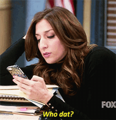 A Woman Sitting At A Desk Looking At Her Phone With The Caption Who Dat GIF