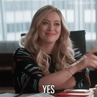 A Woman Sitting At A Desk Says Yes With Her Hands GIF