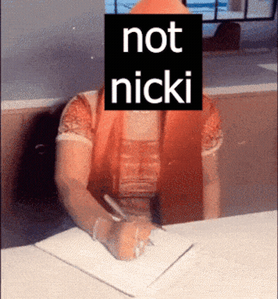 A Woman Sitting At A Desk With A Sign That Says Not Nicki On Her Face GIF