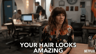 A Woman Sitting At A Desk With The Words " Your Hair Looks Amazing " On The Screen GIF