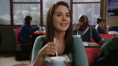 A Woman Sitting At A Table Drinking A Milkshake GIF