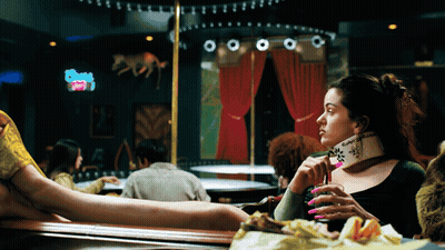A Woman Sitting At A Table In A Bar Holding A Purse That Says ' Swag ' On It GIF