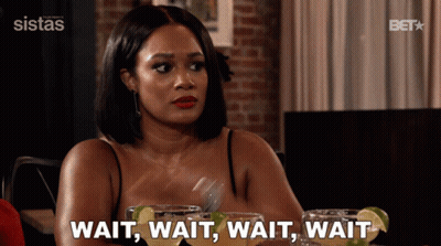 A Woman Sitting At A Table Says Wait Wait Wait Wait While Holding A Fork GIF
