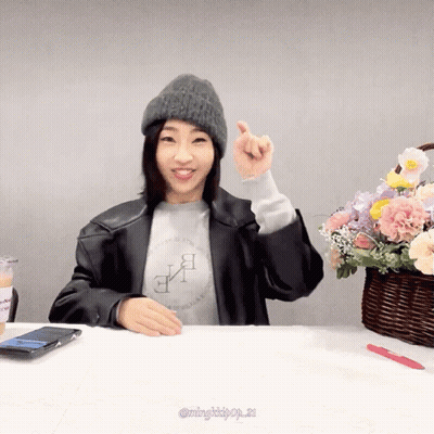 A Woman Sitting At A Table With A Basket Of Flowers GIF