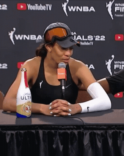 A Woman Sitting At A Table With A Bottle Of Ultra Beer GIF