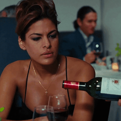 A Woman Sitting At A Table With A Bottle Of Wine That Says " Chateau " On It GIF