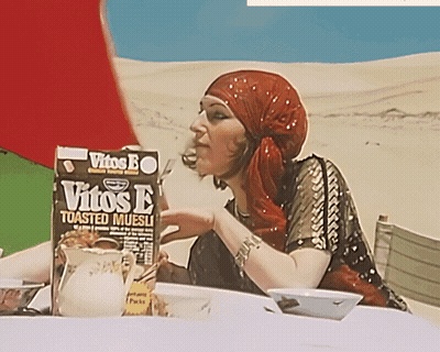 A Woman Sitting At A Table With A Box Of Vitos E Toasted Muesli In Front Of Her GIF