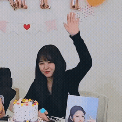 A Woman Sitting At A Table With A Cake And Balloons Behind Her With A Sign That Says " I Love You " GIF