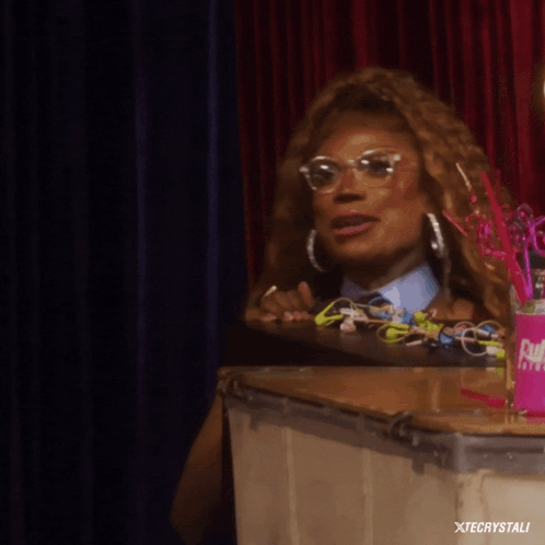 A Woman Sitting At A Table With A Can That Says Xtecrystali In The Corner GIF