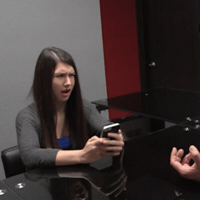 A Woman Sitting At A Table With A Cell Phone In Her Hand GIF