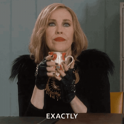 A Woman Sitting At A Table With A Cup In Her Hand And The Word Exactly Written Below Her GIF