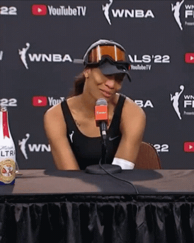 A Woman Sitting At A Table With A Microphone In Front Of A Youtube Tv Wall GIF