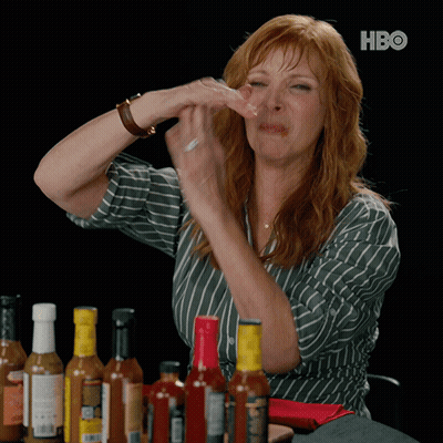 A Woman Sitting At A Table With Bottles Of Hot Sauce And A Hbo Logo On The Bottom GIF