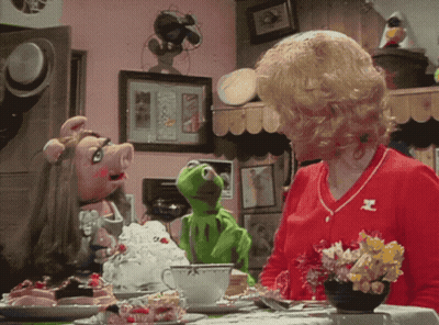 A Woman Sitting At A Table With Muppets Including Kermit GIF