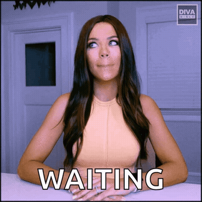 A Woman Sitting At A Table With The Word Waiting Written On The Screen GIF